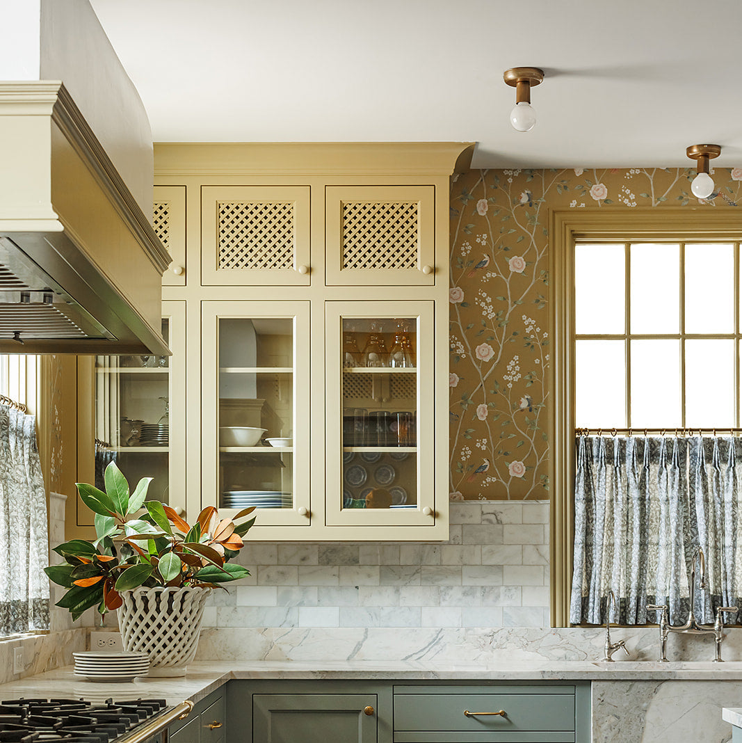 Modern kitchen with green and beige cabinets, marble countertop, and decorative elements.