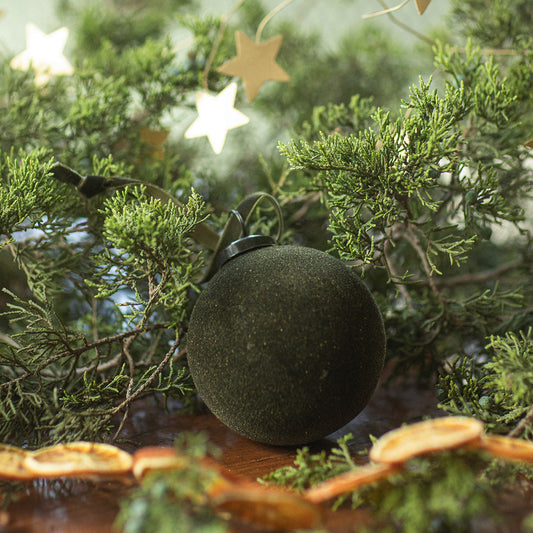 Decorative arrangement with green spherical ornament, star-shaped lights, and dried oranges on a reflective surface.