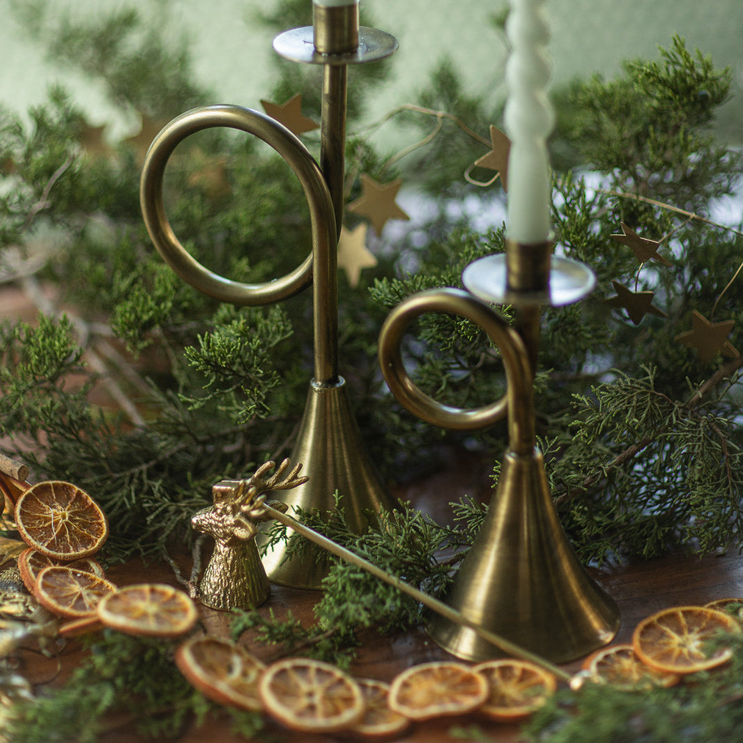 Brass candle holder with white candles on a decorative table setting with greenery and dried oranges.