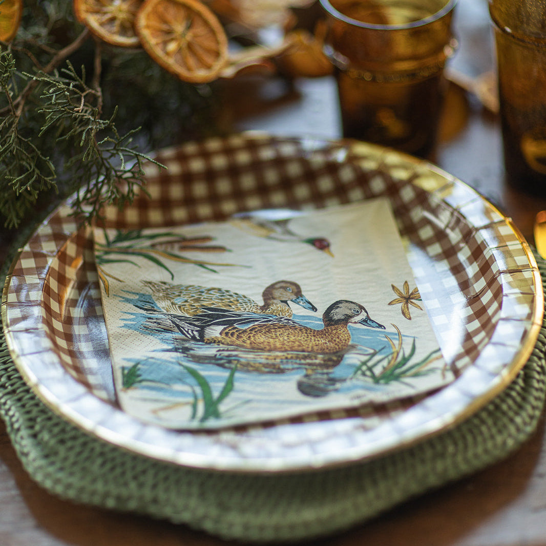 Decorative plate with duck design on a table with checkered napkin and glasses.