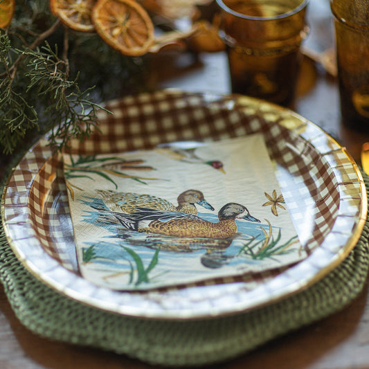 Decorative plate with duck design on a table with checkered napkin and glasses.