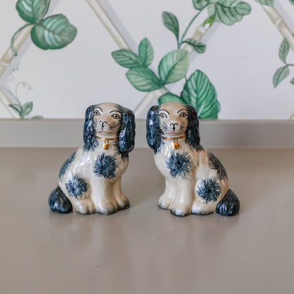 Two ceramic dog figurines on a flat surface with a decorative wall in the background.