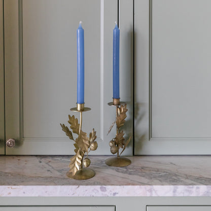 Two gold candle holders with blue candles on a marble surface in front of gray cabinets.