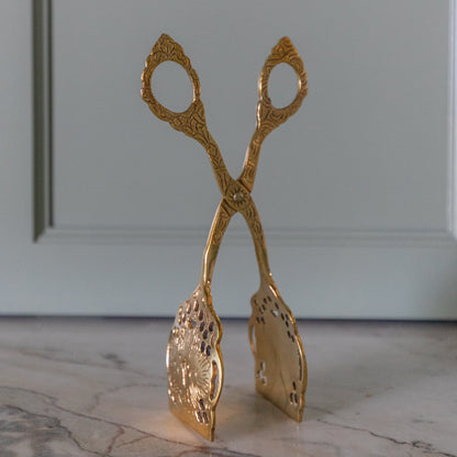 Decorative gold tongs on a marble surface with a gray wall background