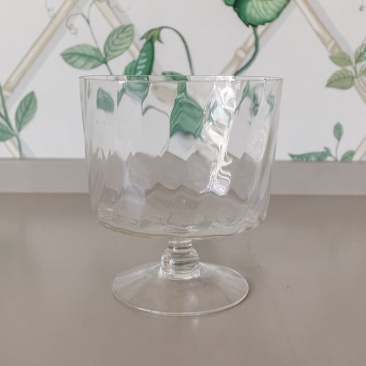 Clear glass with green leaf patterns on a surface with a decorative leaf-patterned wall in the background.