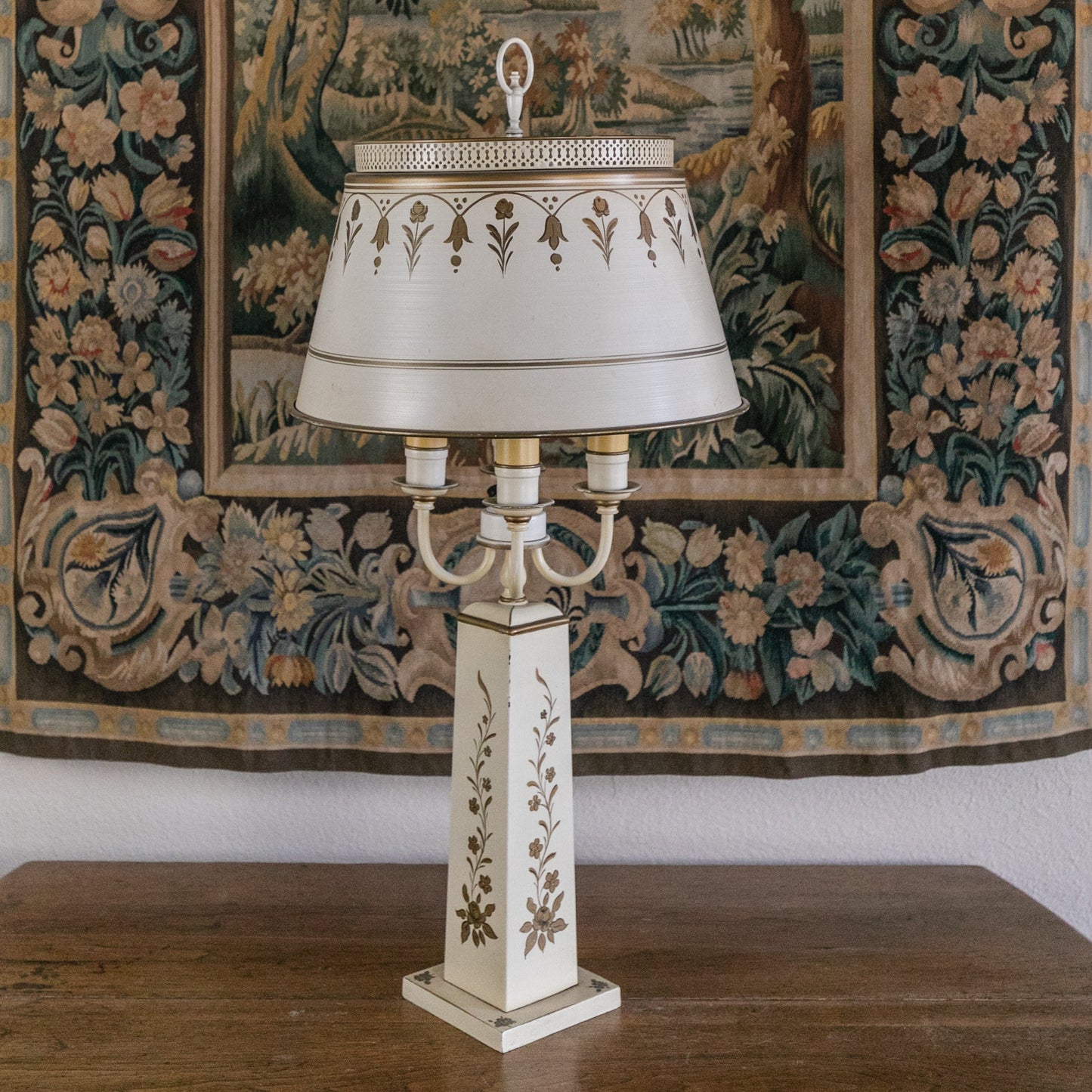 Decorative lamp with intricate design on a wooden surface in front of a large tapestry.