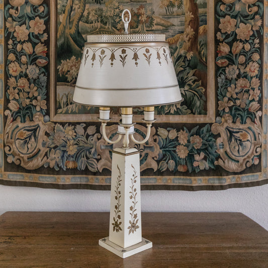Decorative lamp with intricate design on a wooden surface in front of a large tapestry.