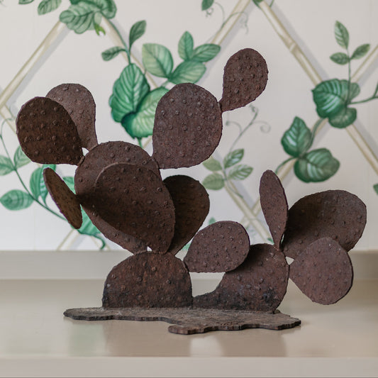 Decorative metal cactus sculpture against a decorative tile wall with green leaves.