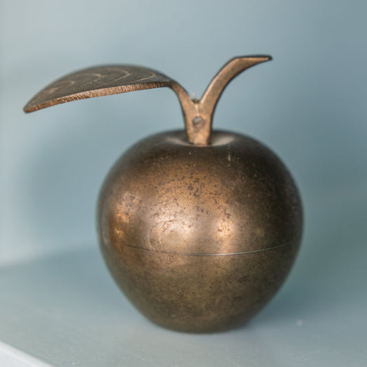 Bronze apple-shaped object with a leaf on a light blue background