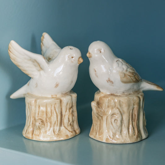 Two ceramic bird figurines on decorative stands against a blue background