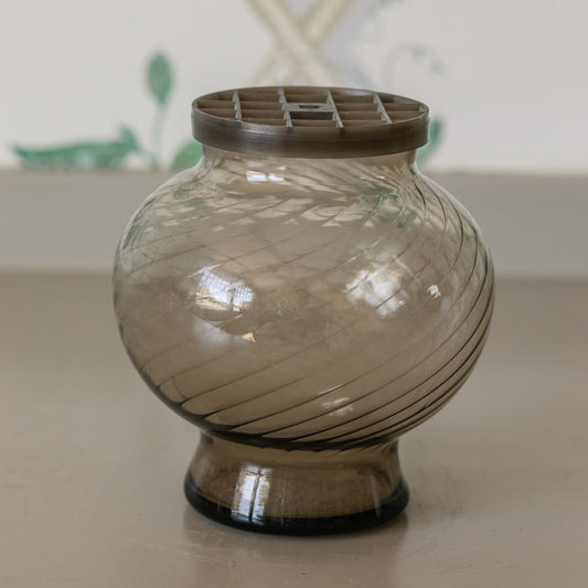 Decorative glass vase with a brown lid on a neutral surface.