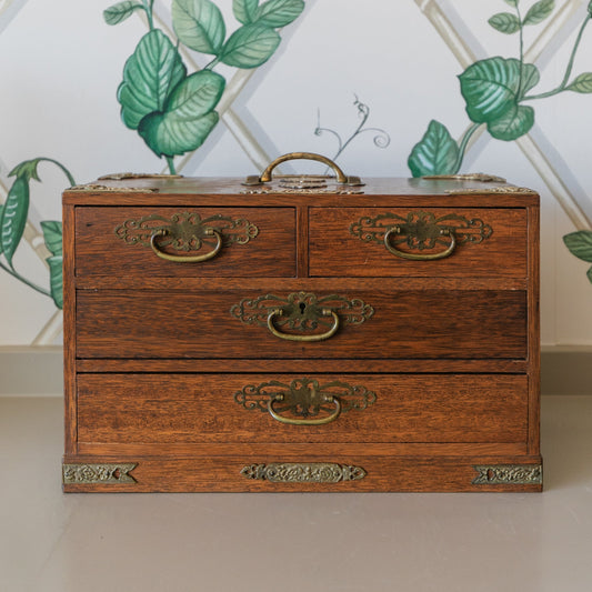 Wooden chest with brass handles against a decorative wall with green leaves.