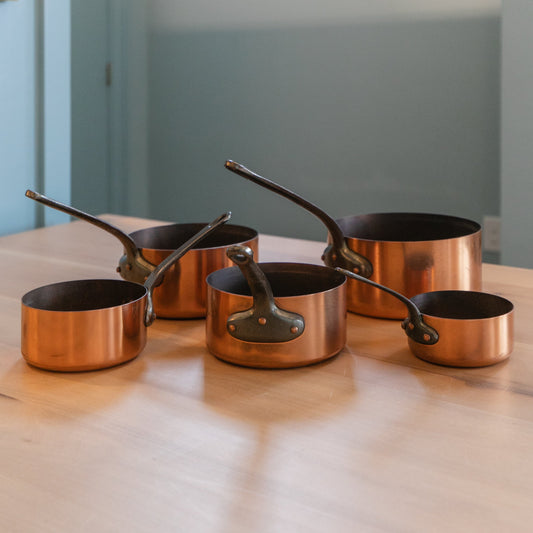 Set of copper cookware on a wooden surface with a neutral background