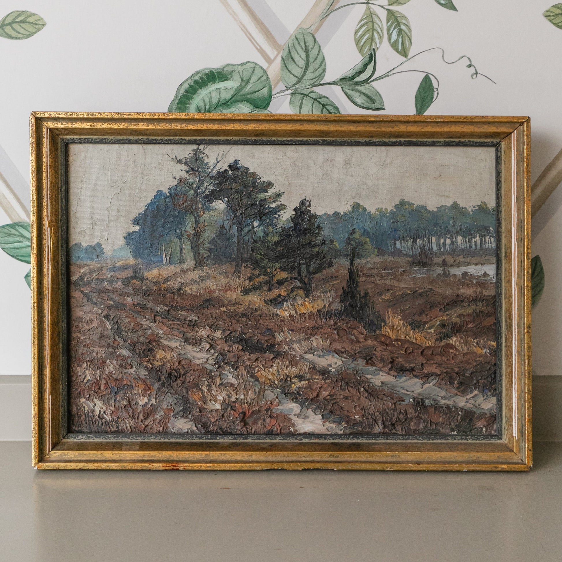Framed landscape painting on a wall with decorative leaves.