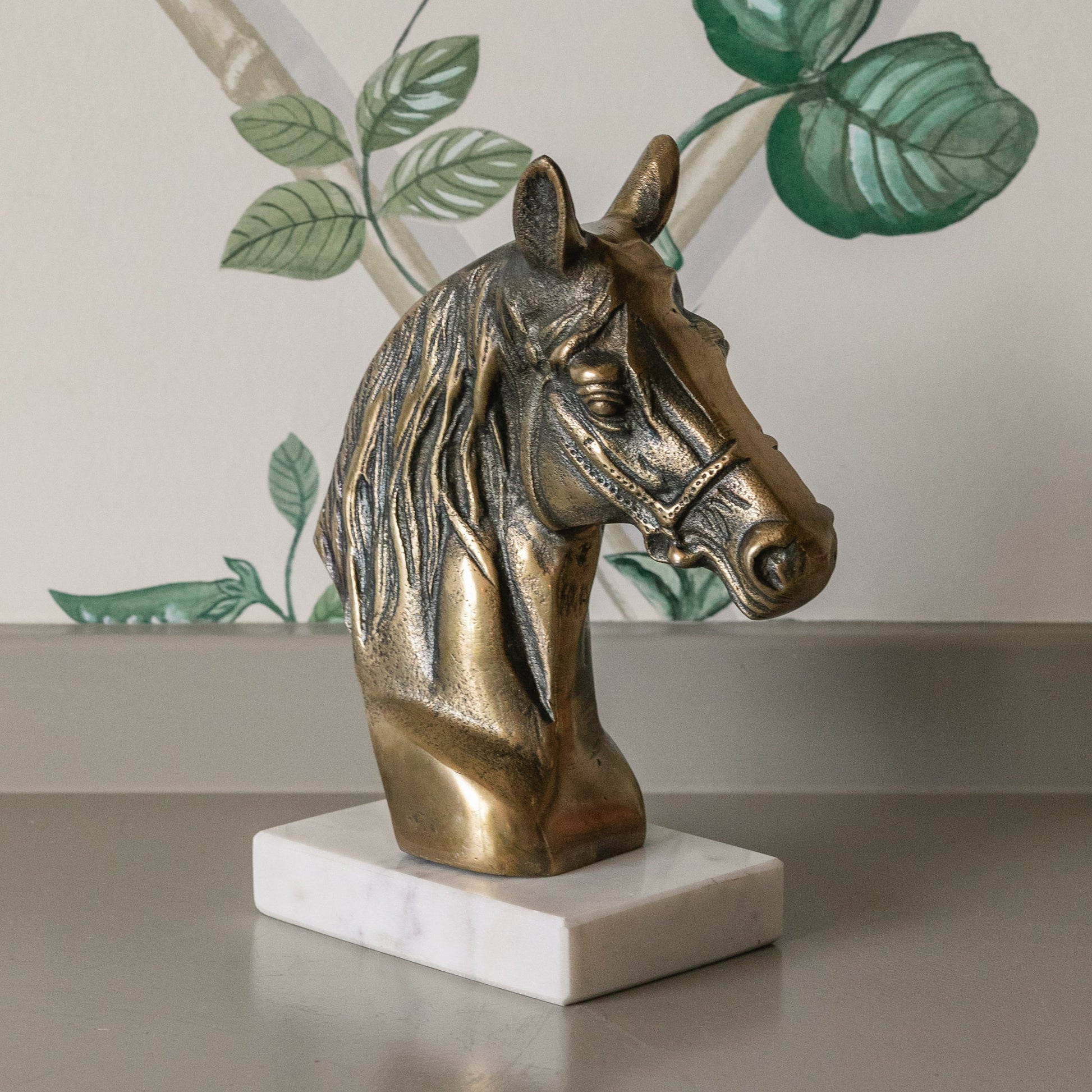 Bronze horse head sculpture on a white marble base with a decorative wall in the background