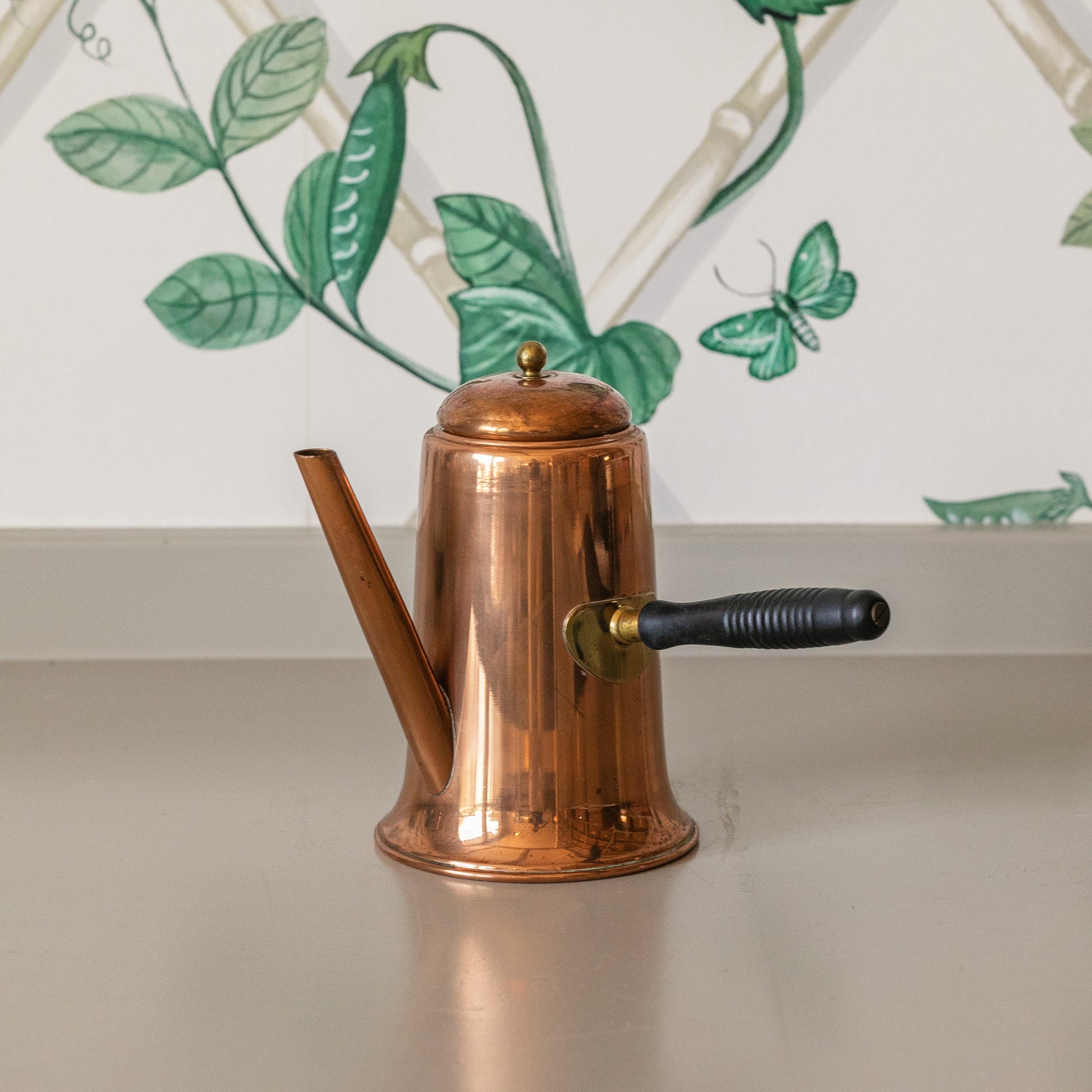 Copper kettle on a countertop with a decorative green leaf pattern in the background