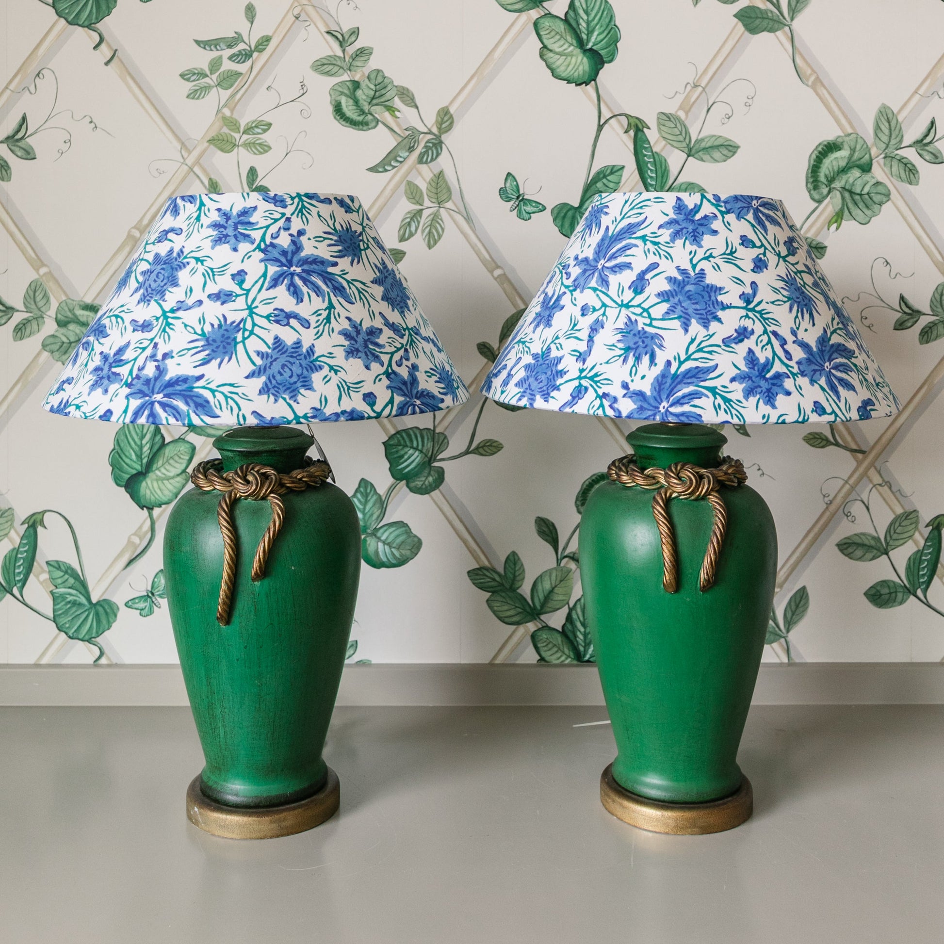 Two green lamps with floral lampshades against a decorative wallpaper background.