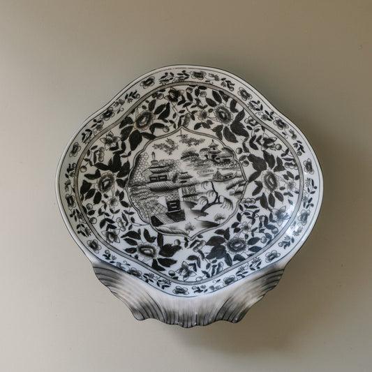 Decorative ceramic plate with black floral patterns on a beige wall