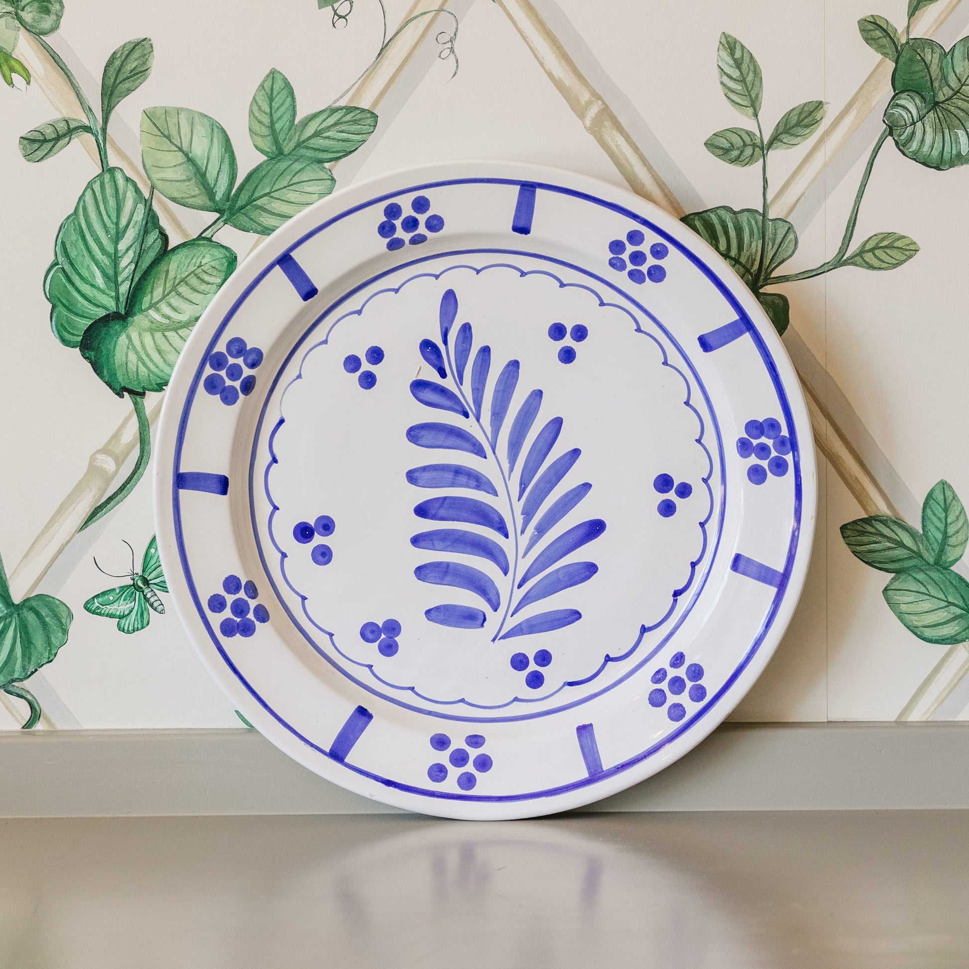 Ceramic plate with blue floral design on a decorative wall with green leaves.