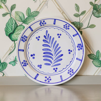 Ceramic plate with blue floral design on a decorative wall with green leaves.