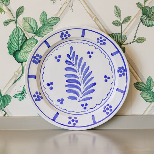Ceramic plate with blue floral design on a decorative wall with green leaves.