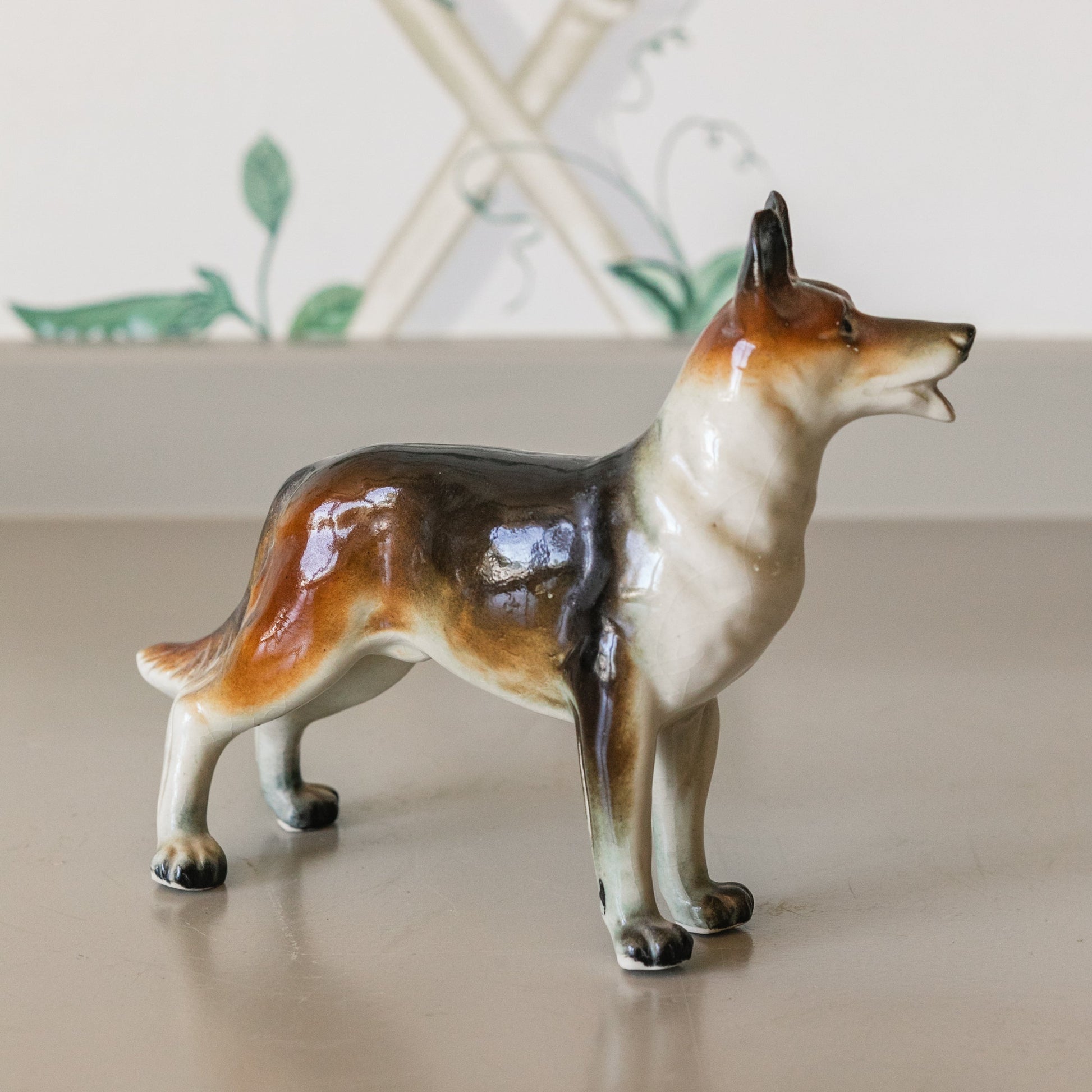 Dog figurine on a reflective surface with a decorative plant in the background